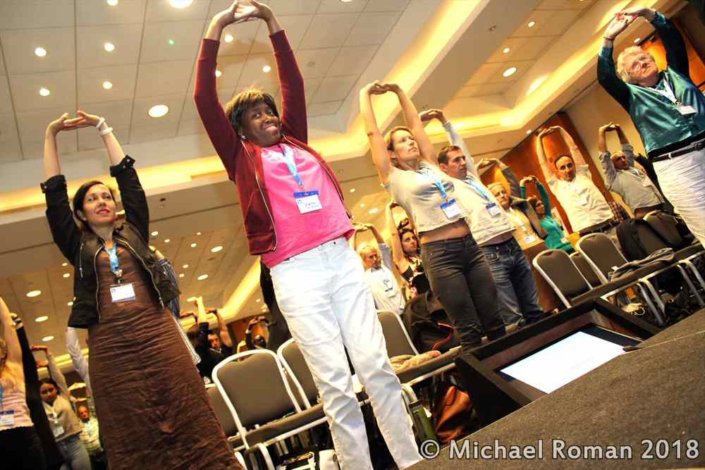 Audience doing a standing posture correction exercise during a workshop