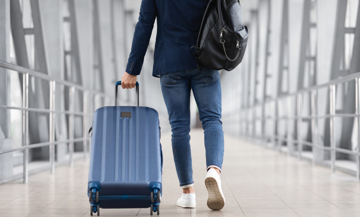 Man walking with suitcase in airport terminal, back view – posture-focused travel preparation