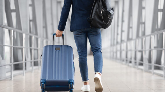Man walking with suitcase in airport terminal, back view – posture-focused travel preparation