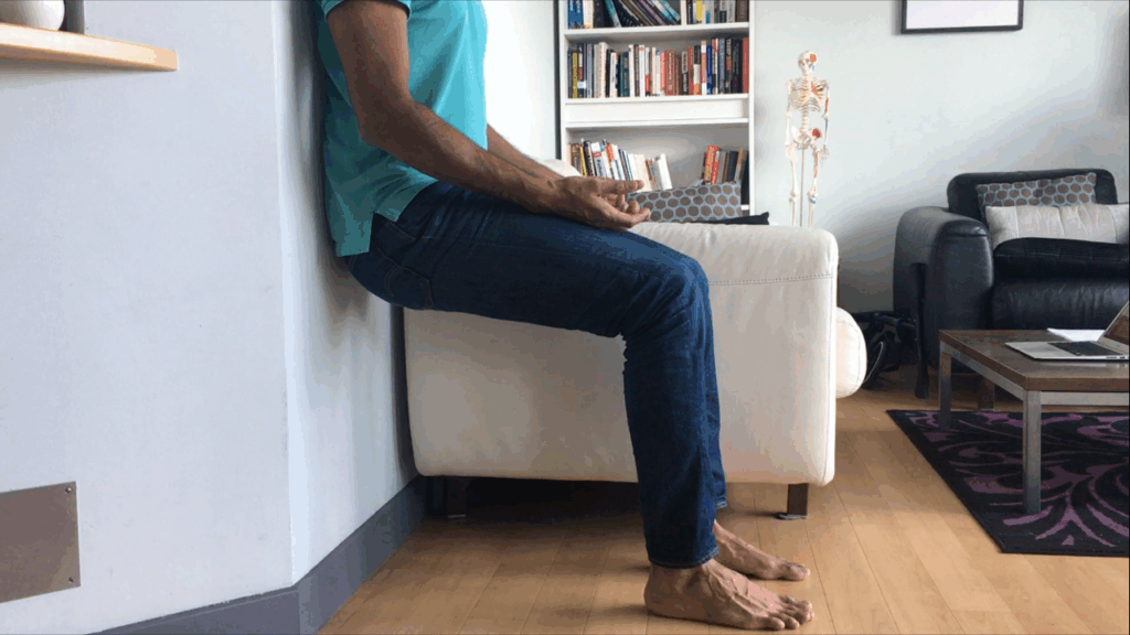 Man performing Air Bench posture correction exercise against wall to help realign hips, spine, and pelvis