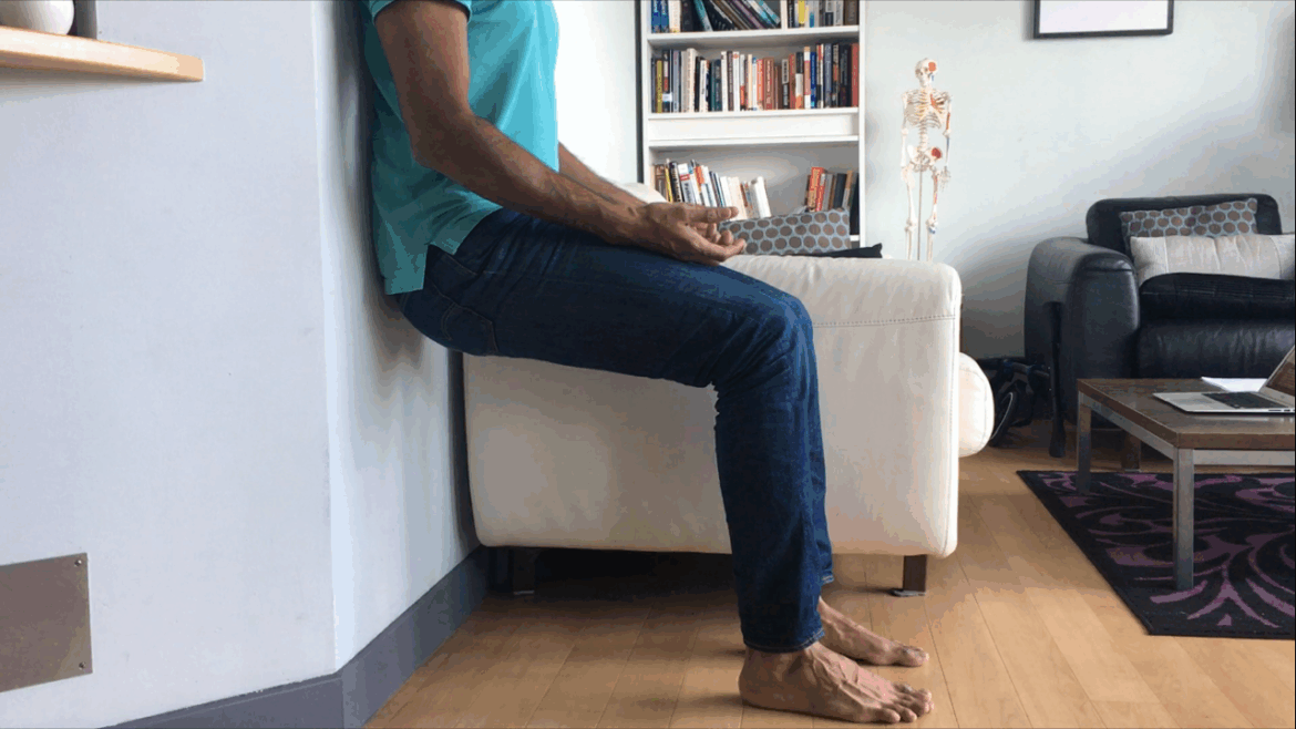 Man performing Air Bench posture correction exercise against wall to help realign hips, spine, and pelvis