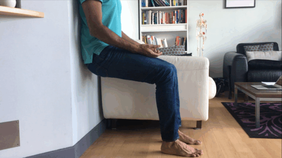 Man performing Air Bench posture correction exercise against wall to help realign hips, spine, and pelvis