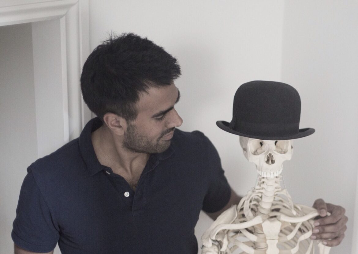 Ameet Bhakta, posture specialist in London, standing next to skeleton model at his clinic