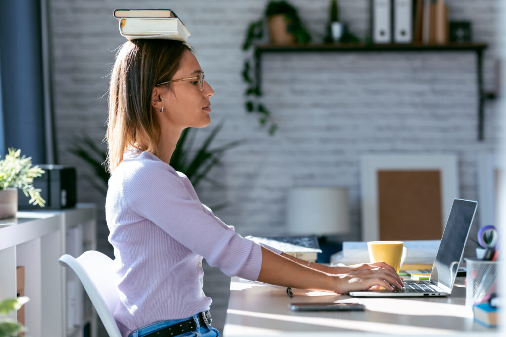 Woman balancing books on her head while working at a desk – trying to improve posture with traditional tips