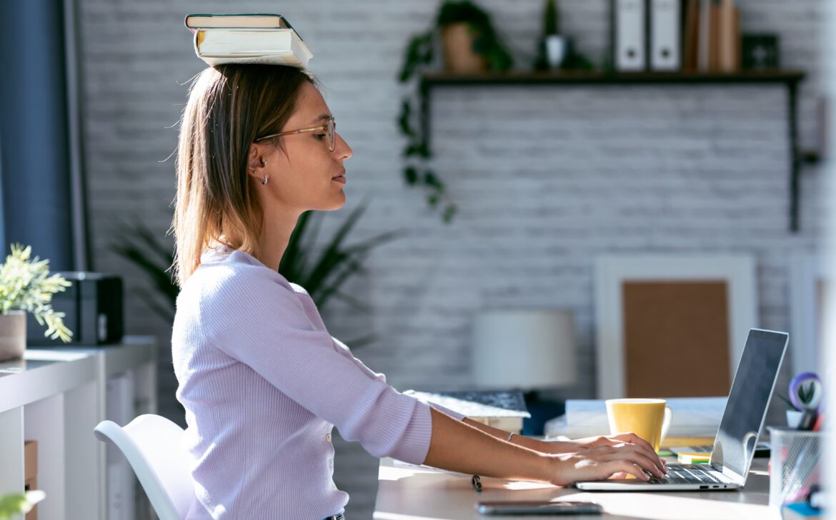 Woman balancing books on her head while working at a desk – trying to improve posture with traditional tips
