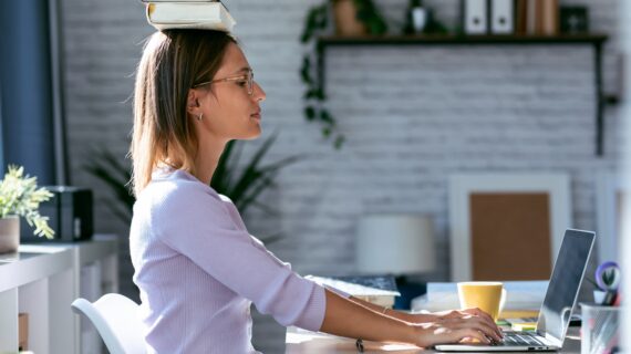 Woman balancing books on her head while working at a desk – trying to improve posture with traditional tips