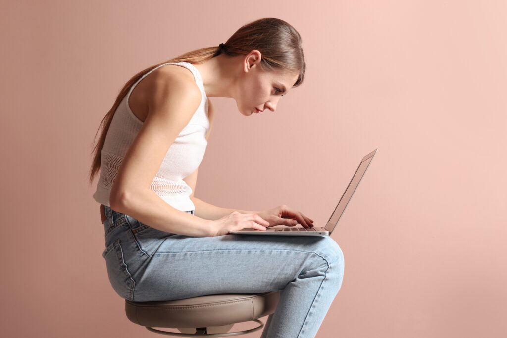 Woman with poor posture hunched over a laptop, showing rounded shoulders and forward head position.