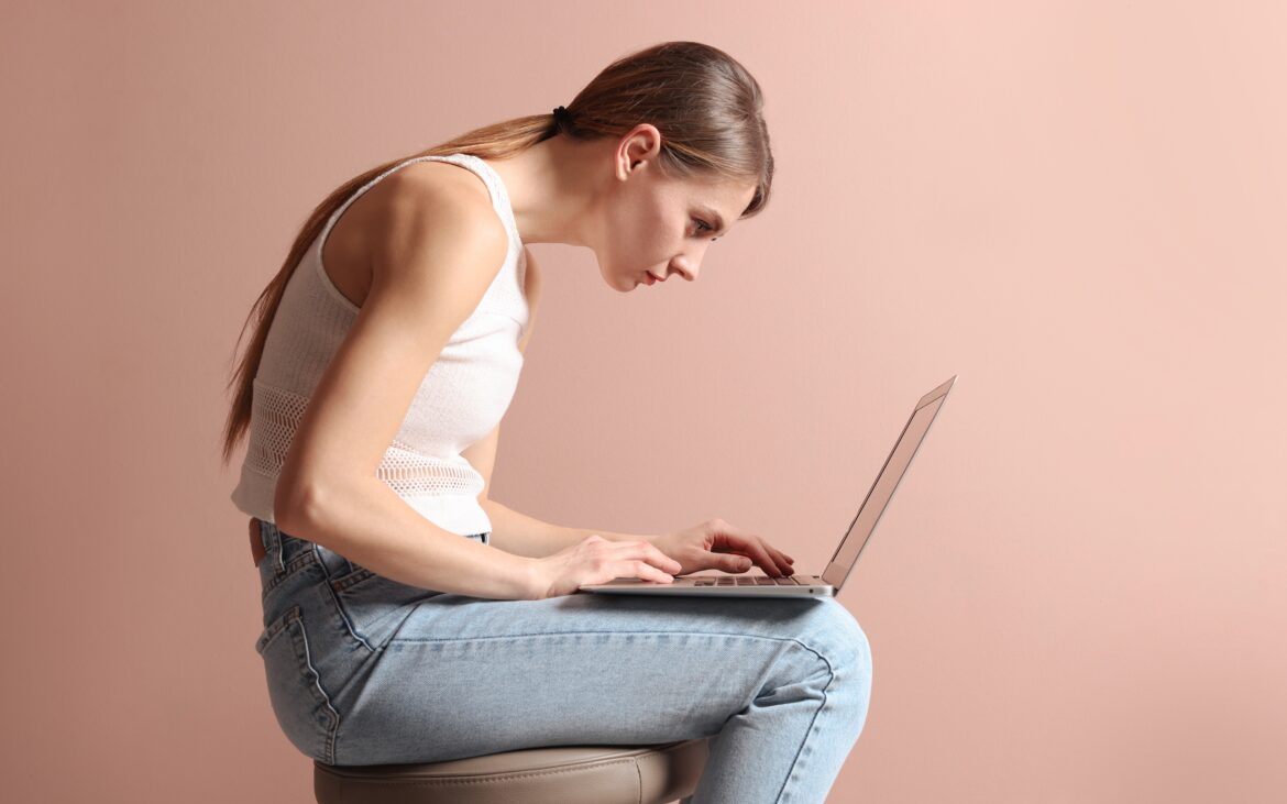 Woman with poor posture hunched over a laptop, showing rounded shoulders and forward head position.