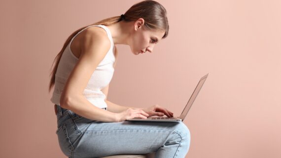 Woman with poor posture hunched over a laptop, showing rounded shoulders and forward head position.