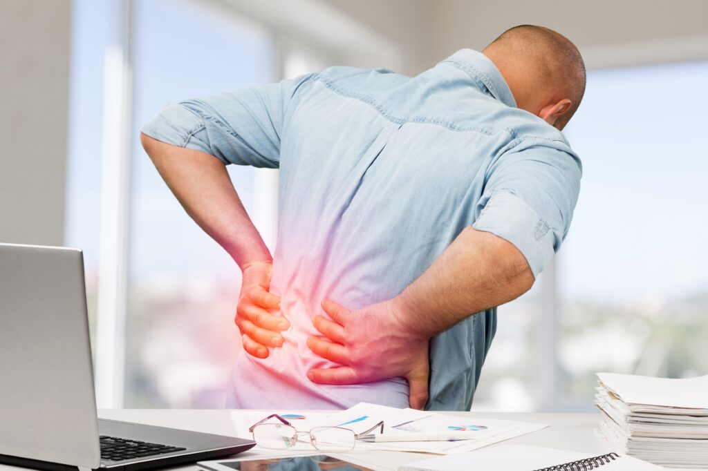 Man in discomfort holding his lower back, symbolising posture-related back pain caused by misalignment