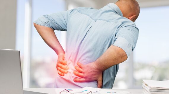 Man in discomfort holding his lower back, symbolising posture-related back pain caused by misalignment