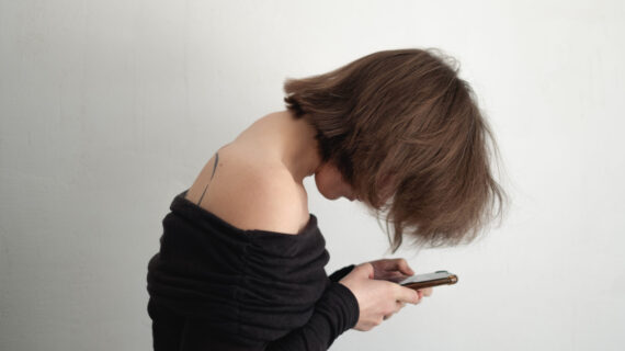 Woman with forward head posture and rounded shoulders looking down at phone, showing visible dowager’s hump