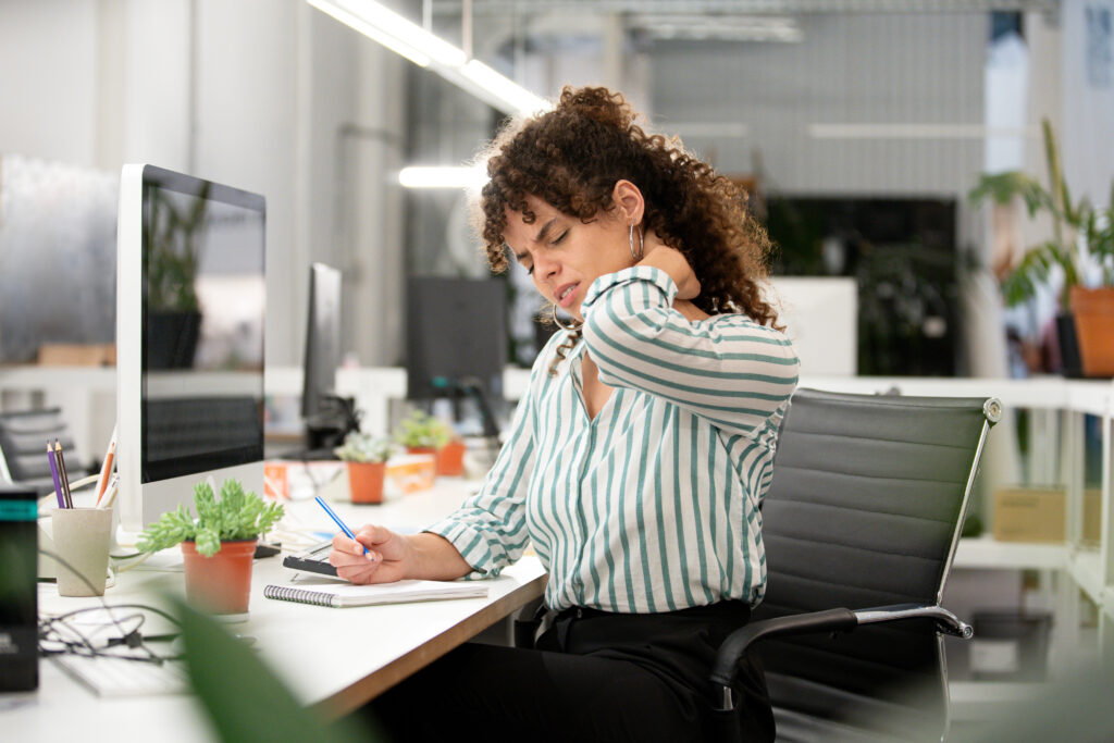 Woman sitting at a desk holding her neck in pain, symbolising posture-related neck tension from office work