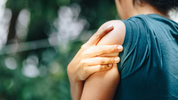 Woman holding her shoulder in pain — highlighting how posture misalignment can contribute to ongoing shoulder issues.